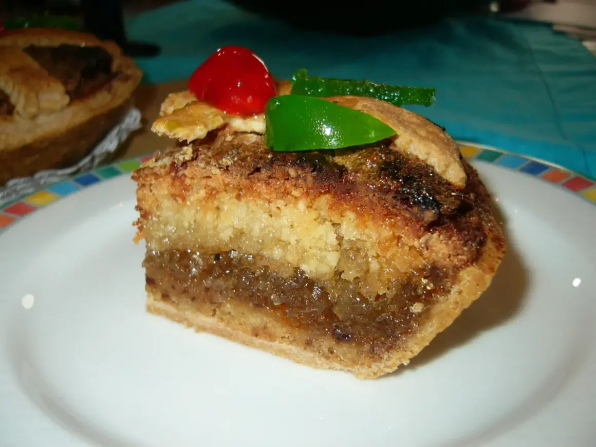 Rebanada de tarta de Mondoñedo, con capas de bizcocho y relleno dulce, decorada con una cereza y un trozo de fruta escarchada verde.
