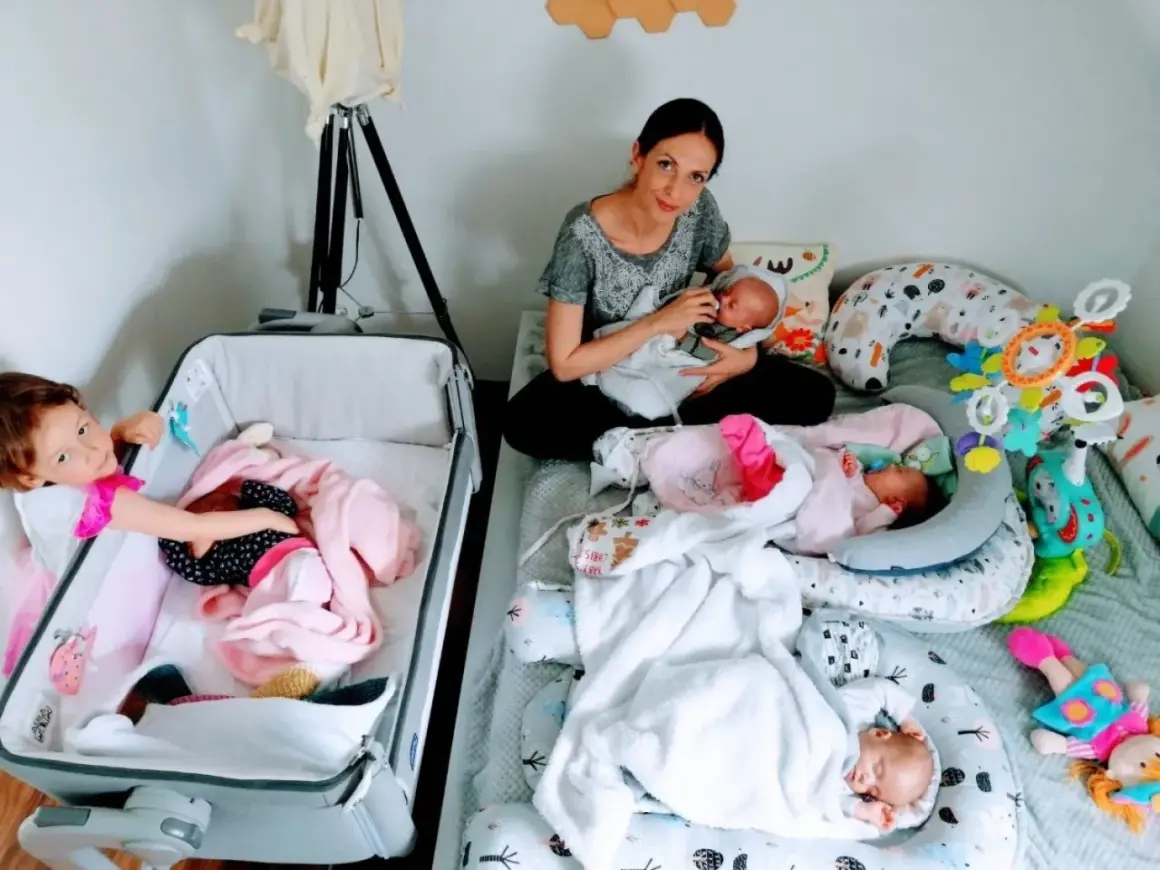 Mama karmi jedno z czworaczków, podczas gdy starsza siostra opiekuje się drugim dzieckiem w łóżeczku.