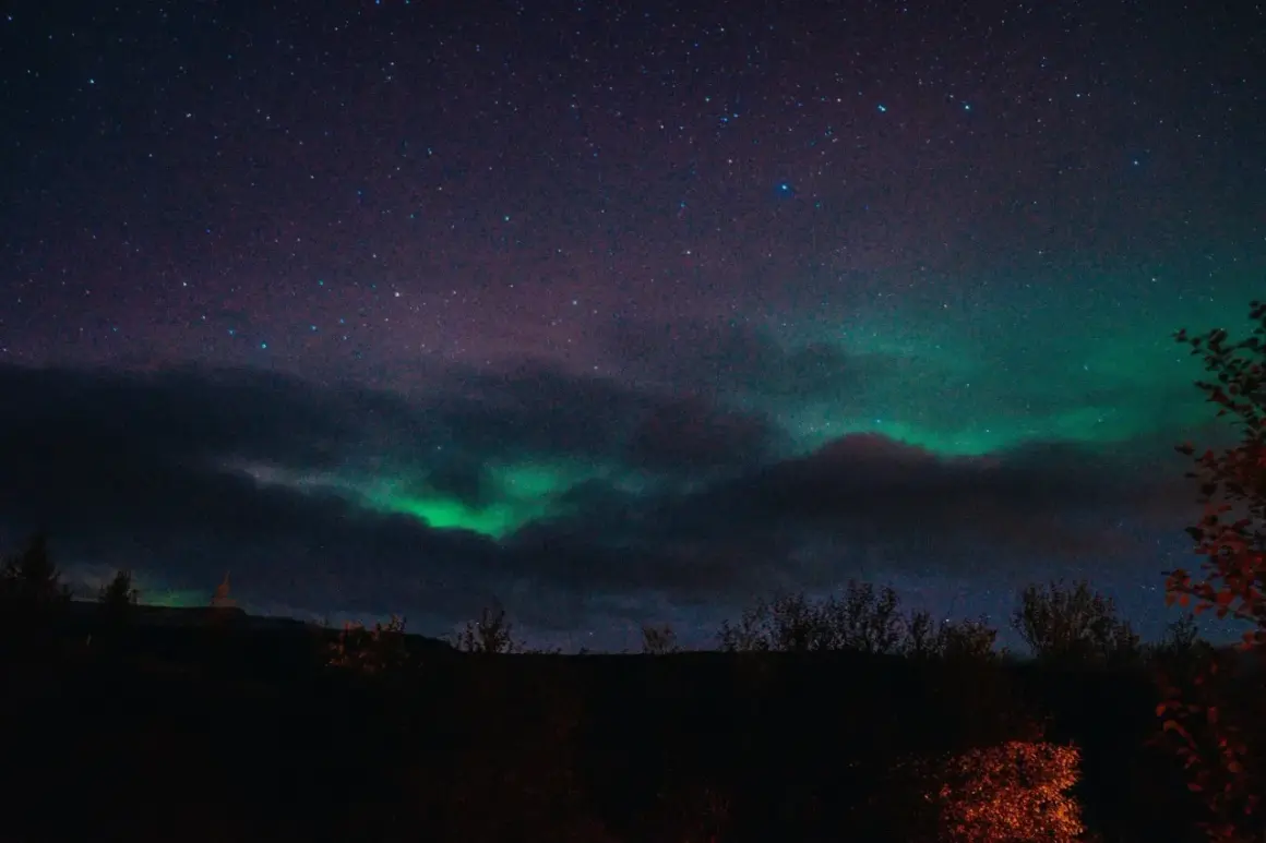 Zielona zorza polarna tańczy na nocnym niebie nad Islandią, wśród gwiazd i ciemnych chmur.