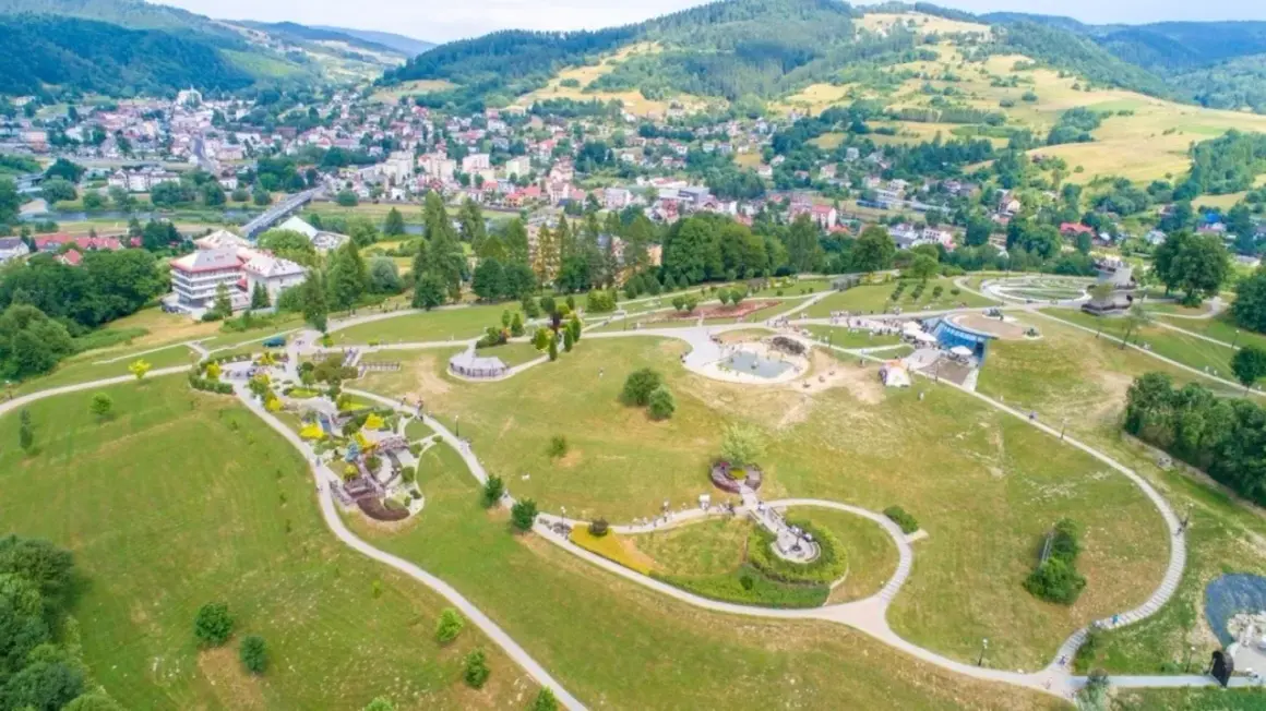 Malowniczy park z alejkami, placem zabaw i wodnymi atrakcjami. W tle widać miasto i góry. To świetne miejsce na rodzinne wycieczki, odkrywając nowe atrakcje Nowego Sącza.