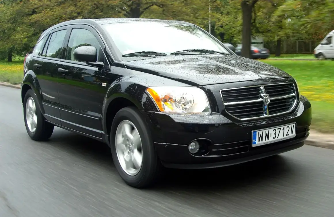 Czarny Dodge Caliber jedzie po mokrej drodze.