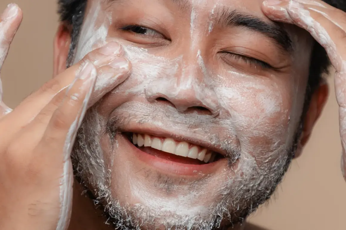 Un visage d'homme souriant, couvert de mousse nettoyante, se fait un soin du visage.