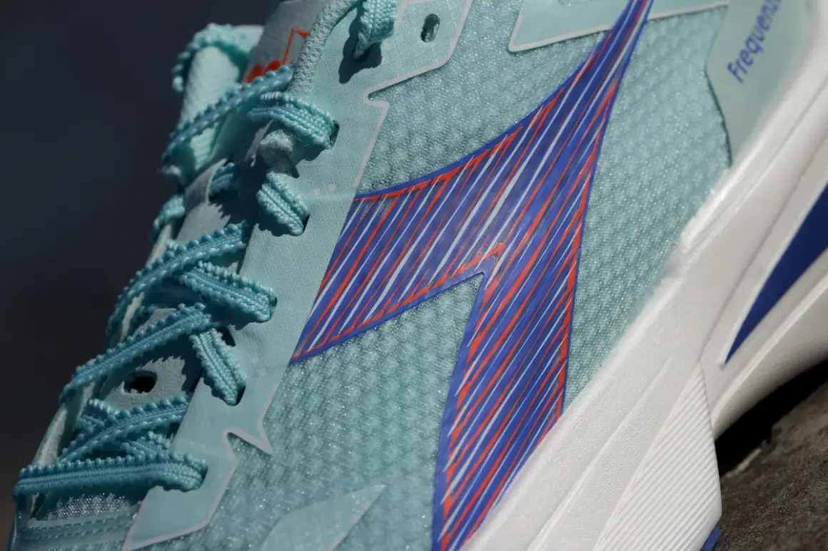 Jasnoniebieskie buty sportowe Diadora Olympia z niebieskimi i pomarańczowymi paskami, idealne na bieżnię.