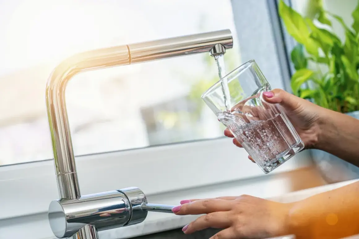 Une main verse de l'eau fraîche du robinet dans un verre. Une idée simple pour comment refroidir de l'eau rapidement.