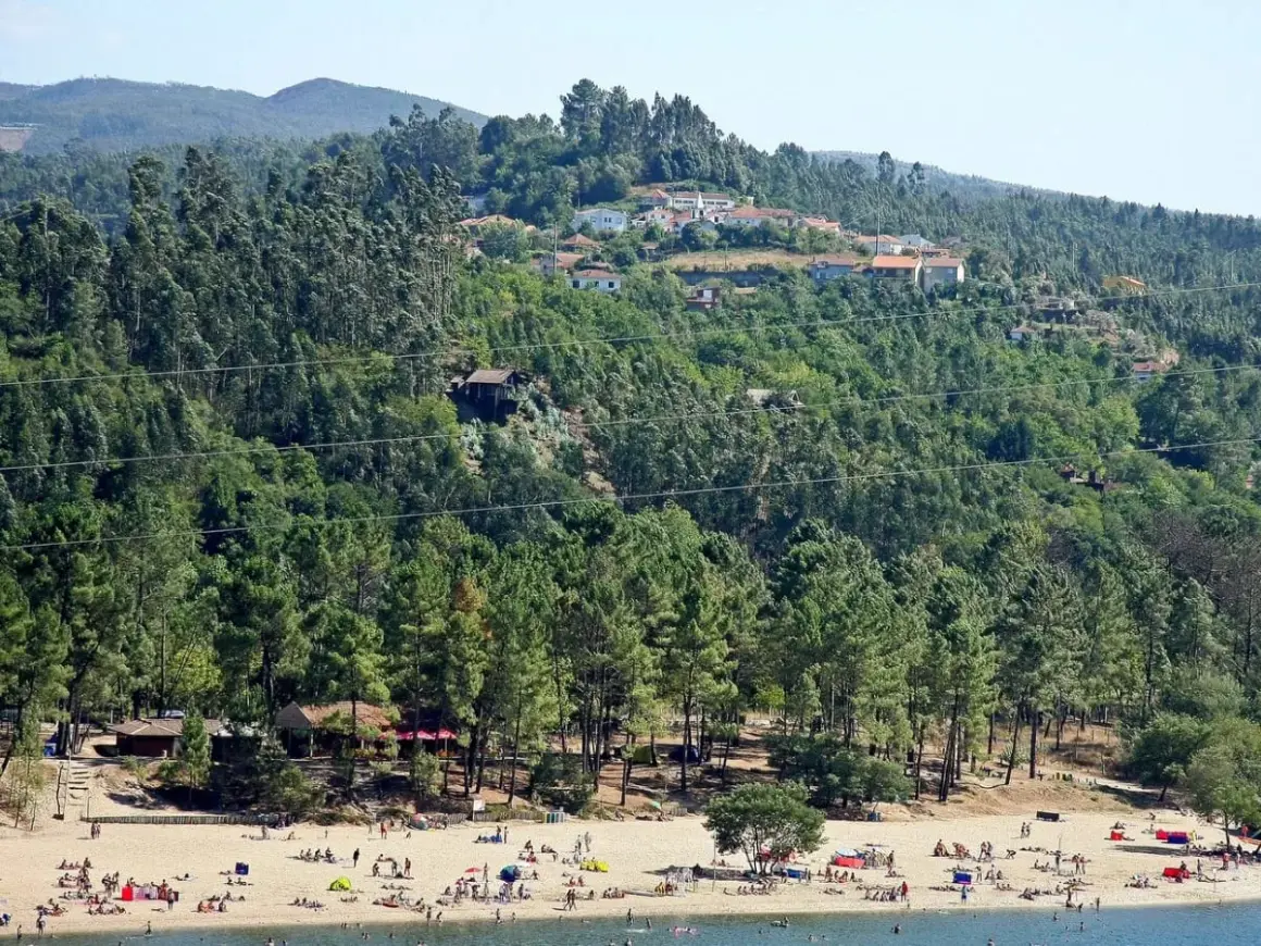 Playa con gente disfrutando del sol y el agua, rodeada de pinos y casas en la ladera. Para saber gondomar como llegar, busca esta idílica estampa.