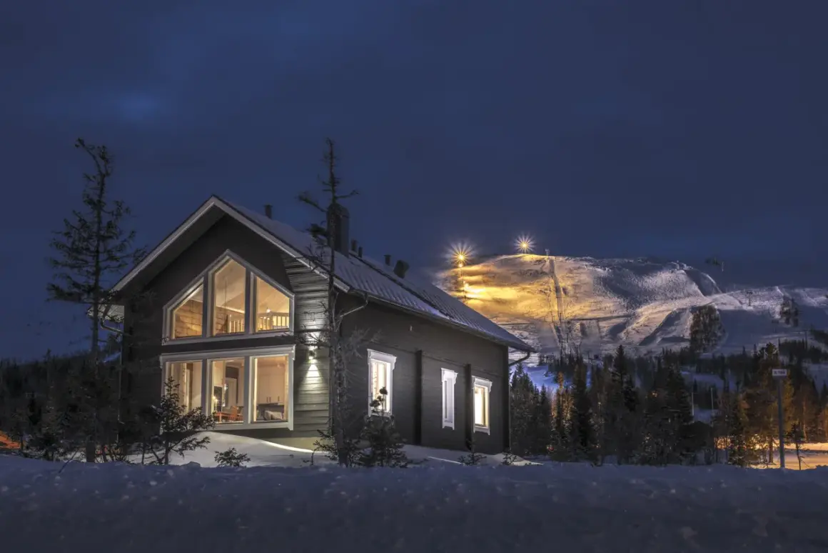 Trillevallen hotell, ett mysigt hus i snölandskap med upplysta skidbackar i bakgrunden.