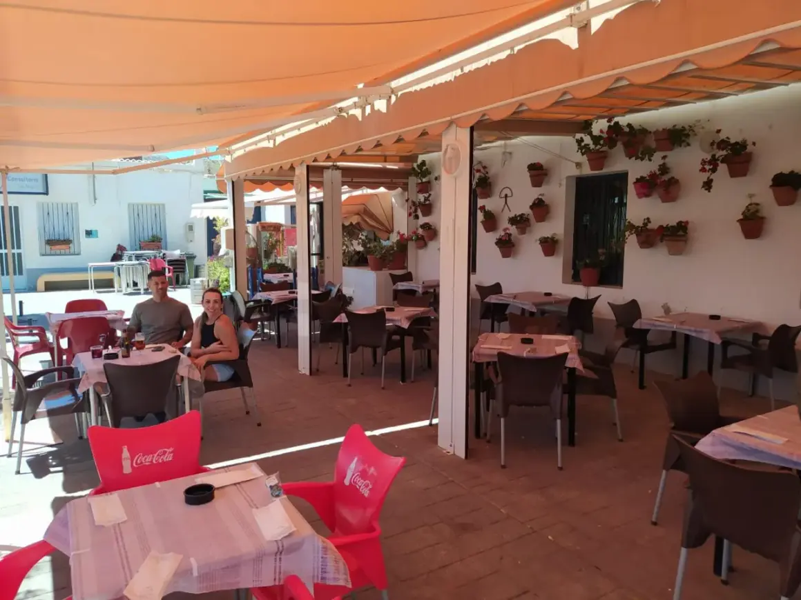 Pareja sonriente en la terraza de "La Chumbera Las Negras", un restaurante con mesas al aire libre y macetas de flores.