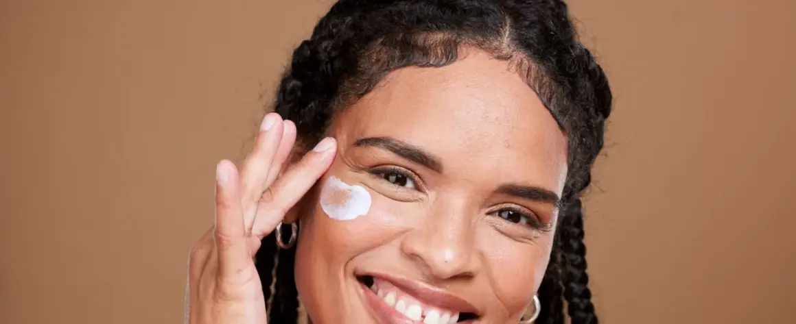 Lächelnde Frau trägt eine Creme auf, die für die vitamin c haut gedacht ist.