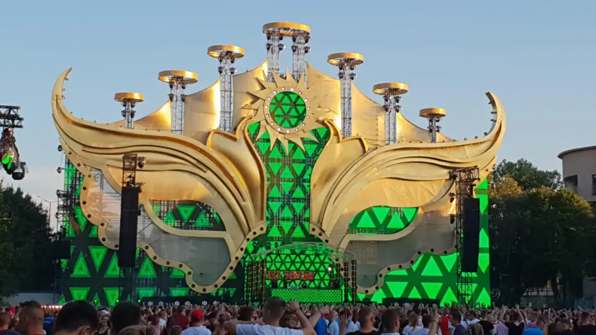 Złota, słoneczna scena festiwalowa z zielonymi światłami, gdzie jest sunrise, otoczona tłumem ludzi.