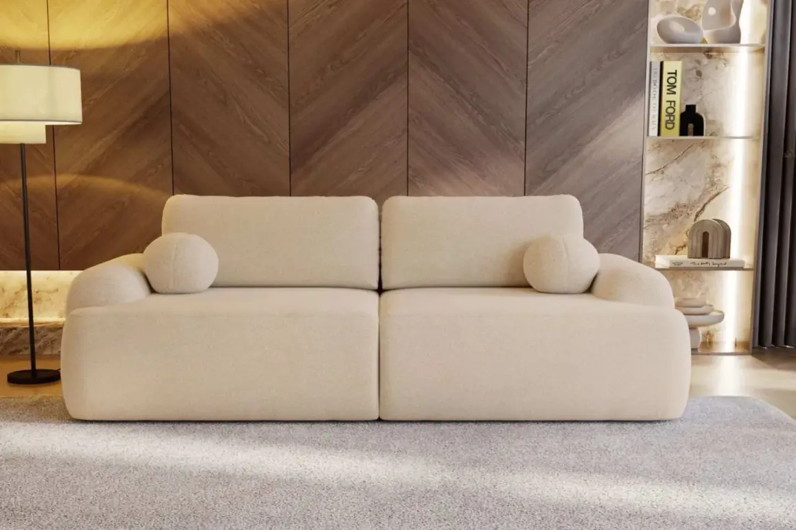 Eine cremefarbene Couch mit runden Kissen, die zum Entspannen einlädt. Sie steht vor einer Holzwand und einem Regal mit Büchern und Deko.