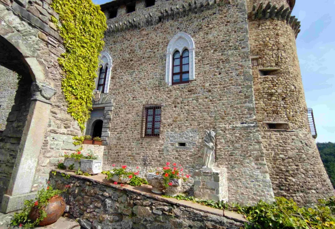 Antica dimora a Compiano, Parma, con mura in pietra, edera rampicante, fiori e una statua.