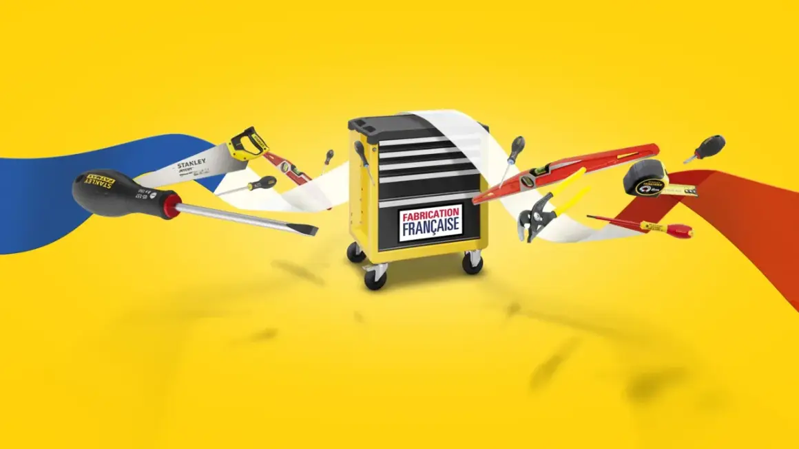 Boîte à outils jaune avec divers outils Stanley, dont une scie, des tournevis et un niveau. Le logo "Fabrication Française" est visible.