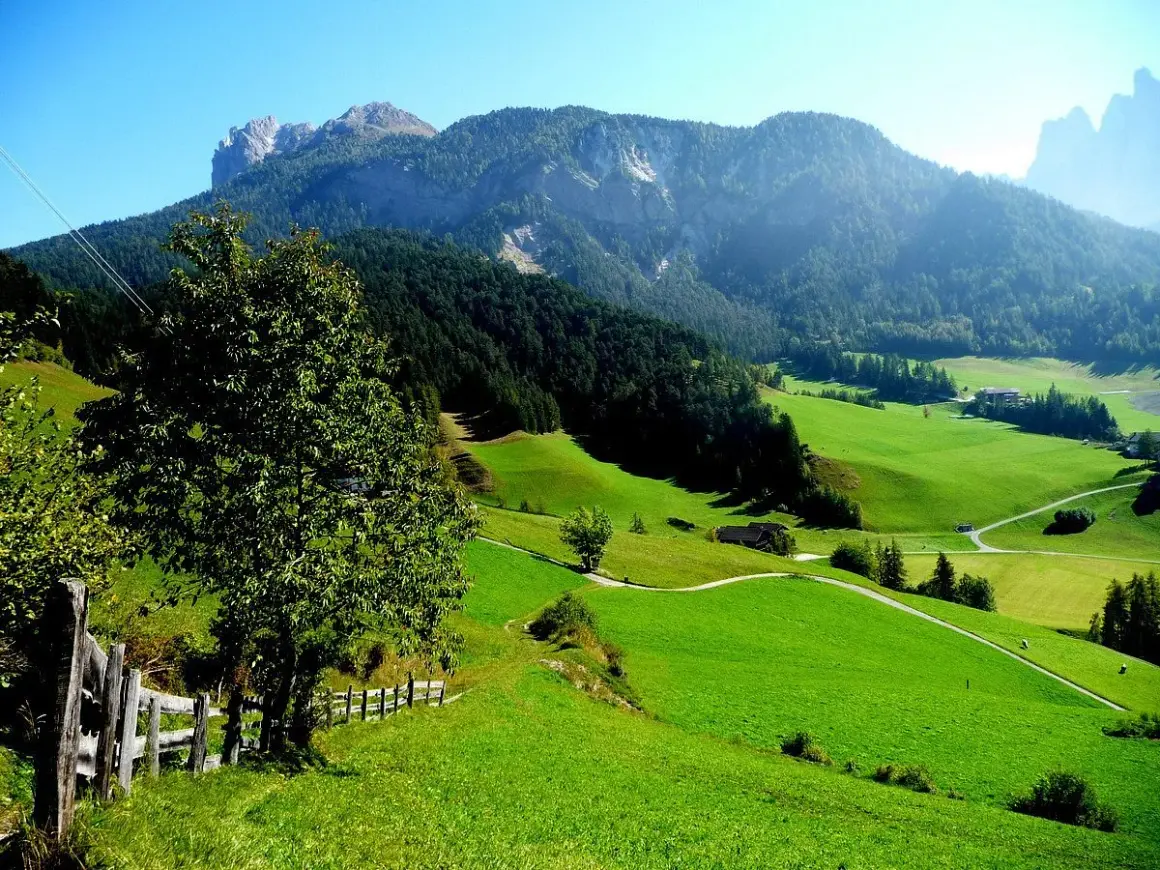 Verdi colline e montagne maestose incorniciano i pittoreschi paesi del Val di Funes, con un sentiero che serpeggia tra prati lussureggianti.