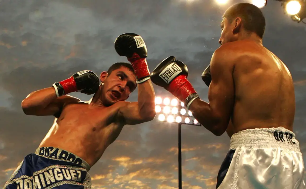 Two boxers clash in a dramatic boxing round, sweat flying as they exchange blows under stadium lights.