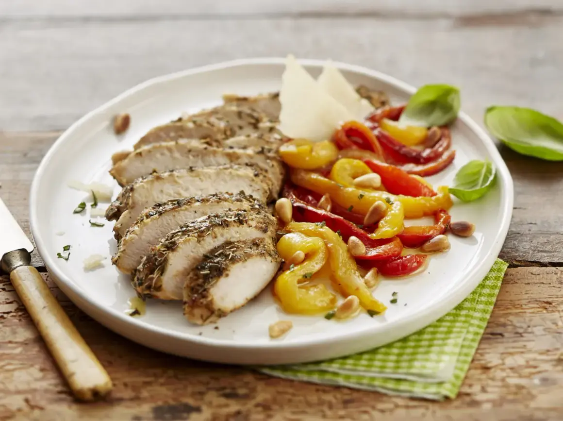 Sabroso pollo con pimientos asados, piñones y queso parmesano, servido en un plato blanco sobre una mesa de madera.