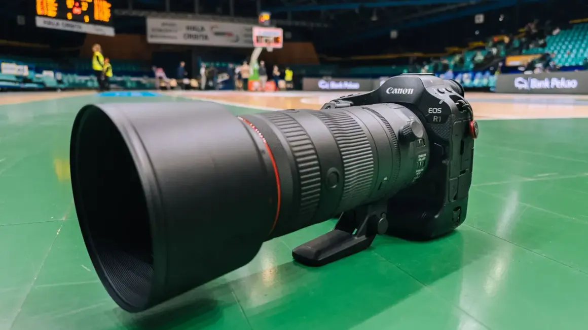 Profesjonalny obiektyw Canon EOS R1 z teleobiektywem 70-200mm na zielonej podłodze hali sportowej.