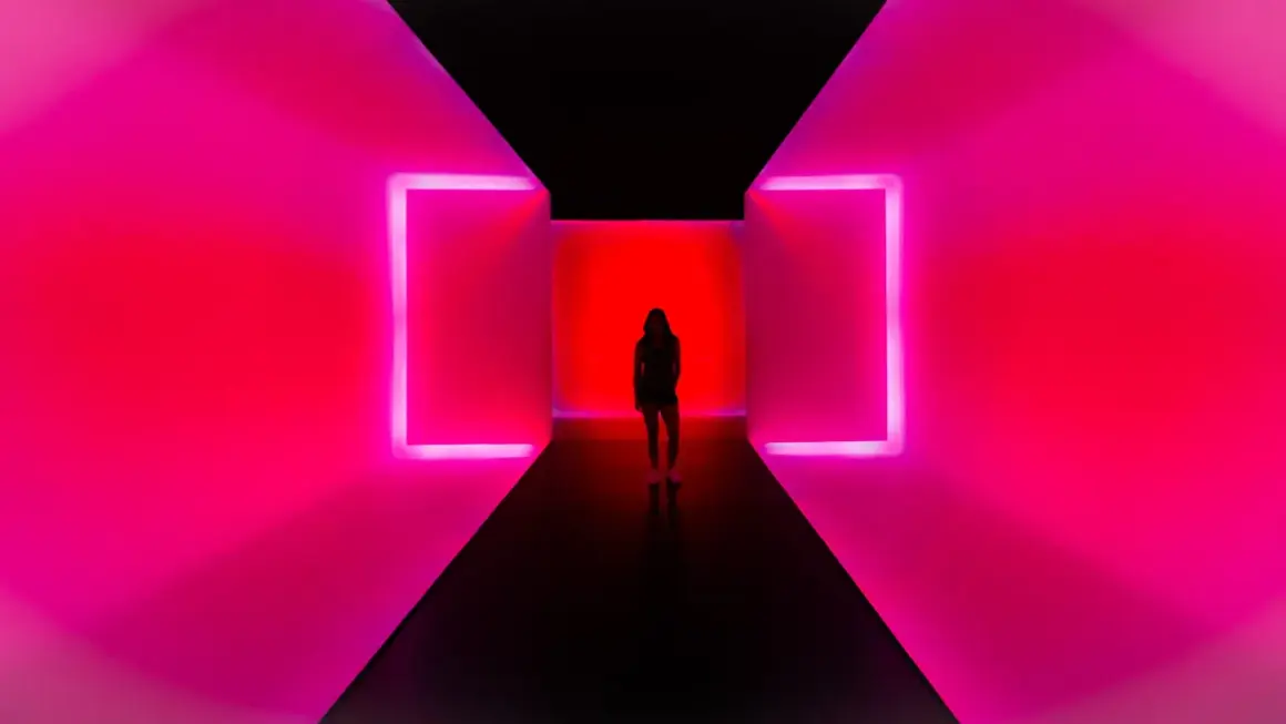 Kobieta stoi w korytarzu z neonowym oświetleniem. To nowoczesne instalacje artystyczne, które tworzą hipnotyzującą grę światła i koloru.