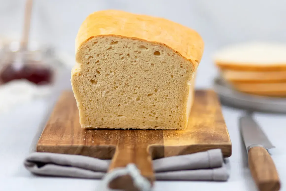 Frisch gebackenes Toastbrot, perfekt für Ihr nächstes Toastbrot Rezept. Auf einem Holzbrett mit Messer und Marmelade im Hintergrund.