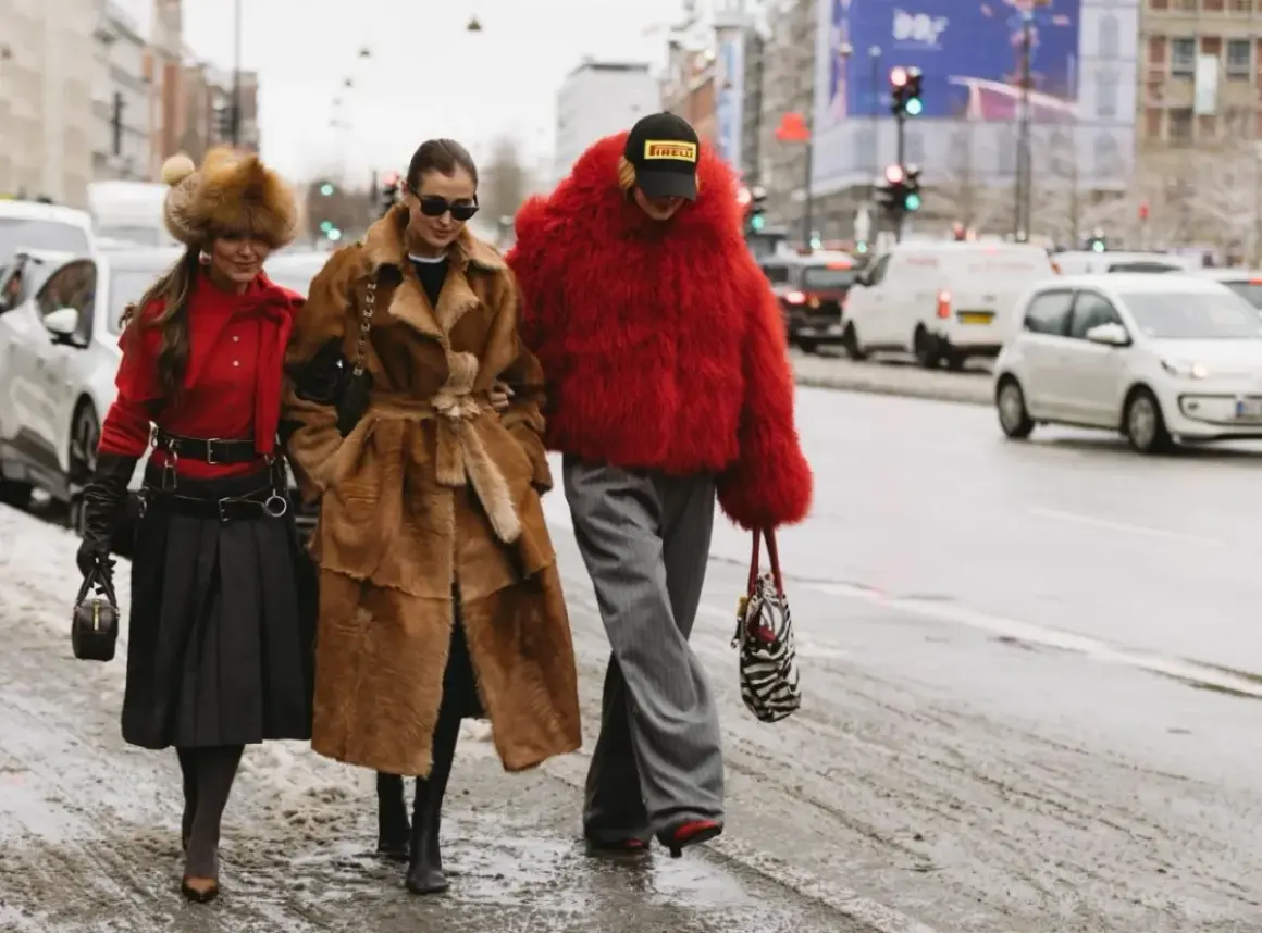Tre kvinnor i trendiga ytterkläder, en med röd pälsjacka, visar upp **copenhagen street style** på en snöig gata.