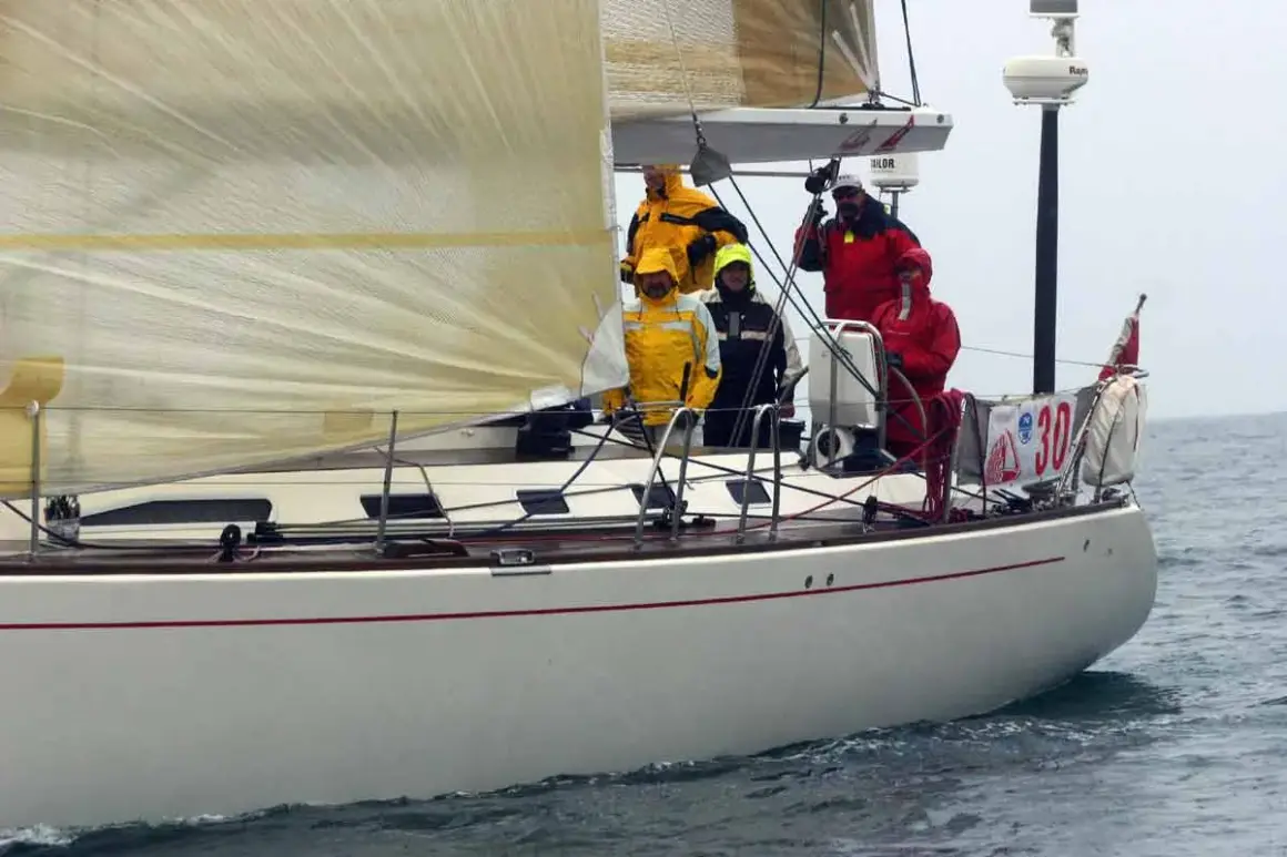 Equipaggio su una barca a vela, con un uomo che sembra D'Alema in giacca gialla.