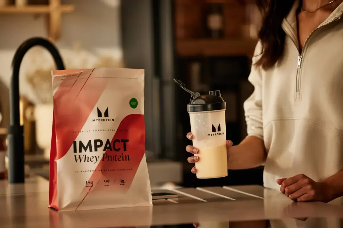 Eine Person hält einen Shaker mit einem cremigen Getränk. Daneben liegt eine Packung Myprotein Impact Whey Protein. Perfekt für den proteinshake vor dem schlafen.