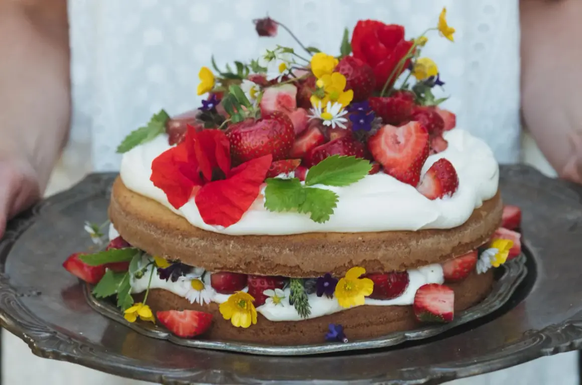 Enkel tårta med vispgrädde, jordgubbar och vilda blommor på ett silverfat.