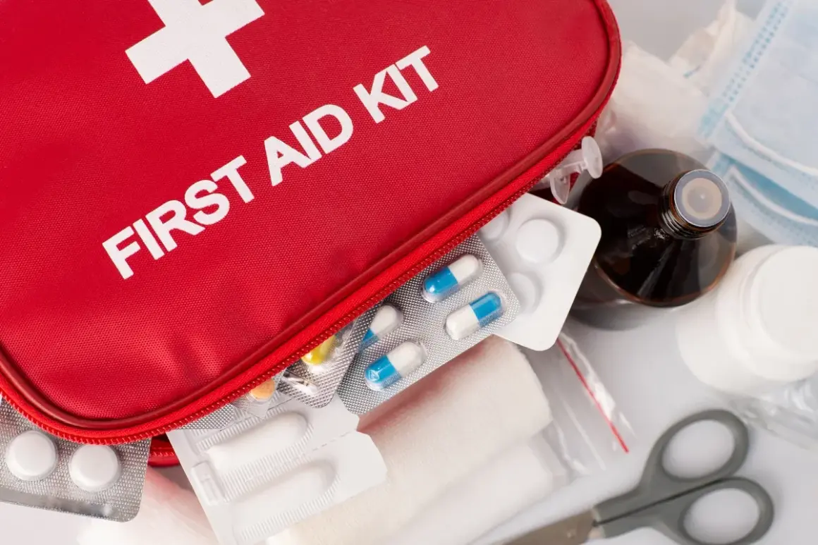 Czerwona apteczka z napisem "FIRST AID KIT", tabletki, bandaże, buteleczka z płynem i maski.