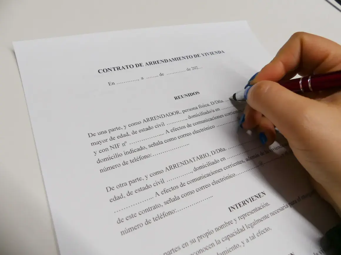 Mano con bolígrafo firmando un contrato de arrendamiento de vivienda. Se detallan los requisitos para alquilar un piso como propietario.