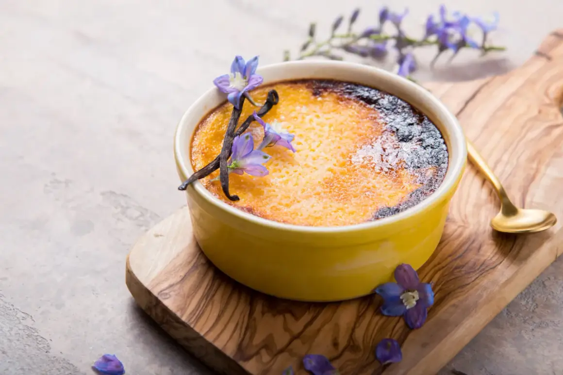 Creme brulee rezept: goldbraune Kruste, Vanilleschoten und blaue Blüten zieren das Dessert auf einem Holzbrett.