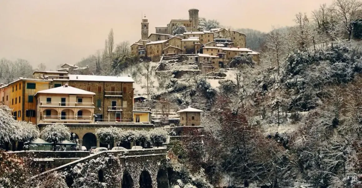 Borgo innevato in Toscana. Case antiche e alberi coperti di neve creano un paesaggio fiabesco, dimostrando che sì, a volte fa neve in Toscana.