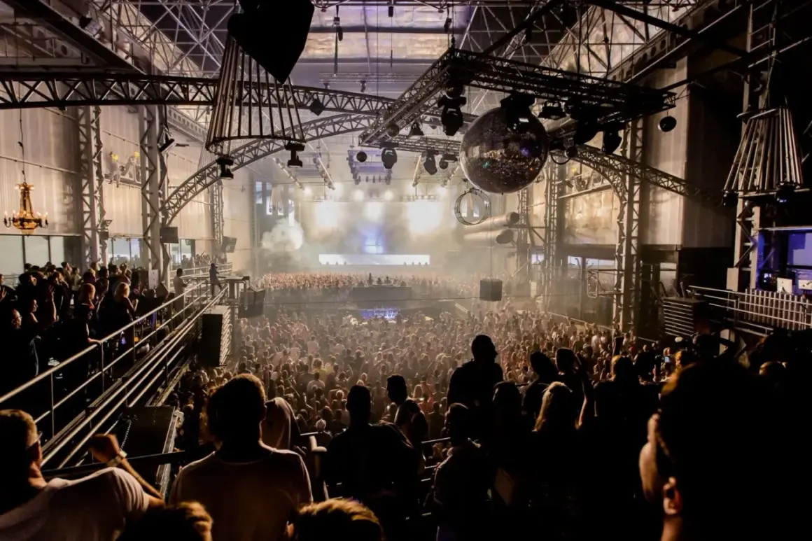 Un'enorme folla balla in una discoteca con luci stroboscopiche e una palla da discoteca scintillante, un'esperienza di **privilege discoteca Ibiza**.