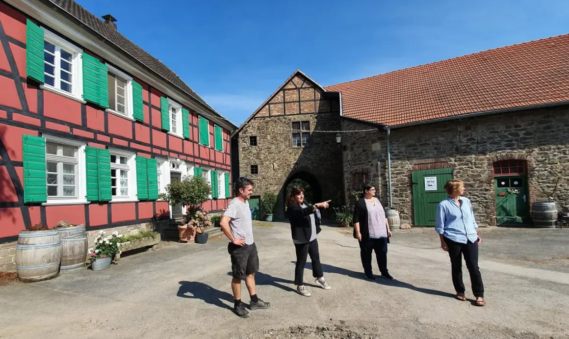 Vier Personen stehen vor einem historischen Fachwerkhaus und einem steinernen Torbogen auf dem Gut Nesselrath.