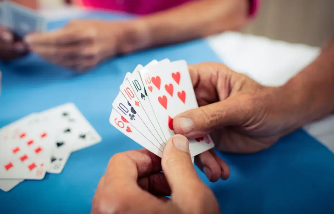Hände halten Spielkarten, ein Spiel zur Förderung der kognitiven Fähigkeiten bei Demenz.
