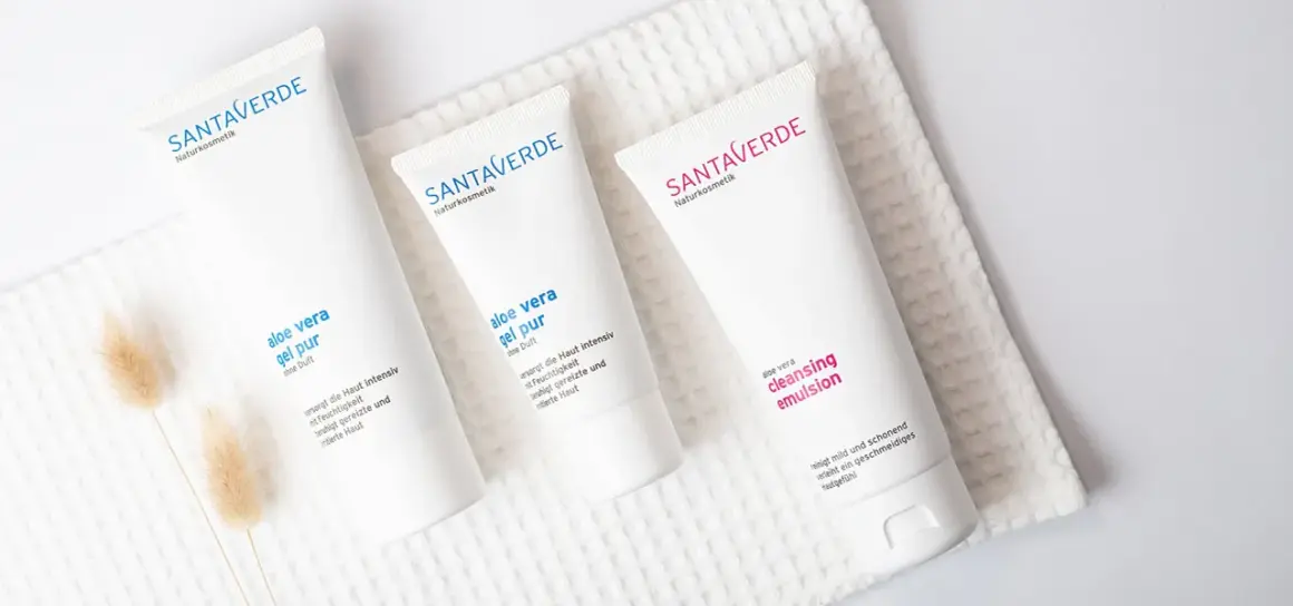 Drei weiße Tuben mit Naturkosmetik, darunter Produkte mit reiner Aloe Vera, liegen auf einem weißen Handtuch.