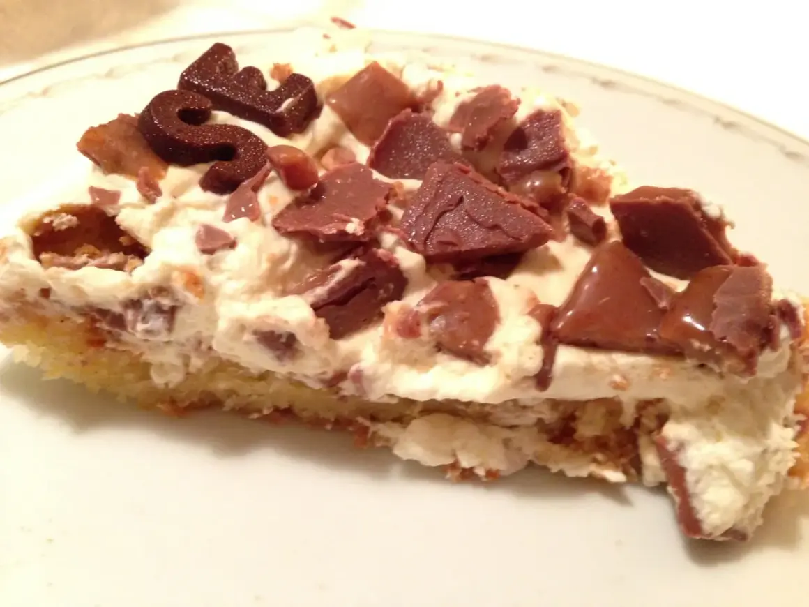 En bit krämig daim tårta med chokladbitar och en chokladdekoration.