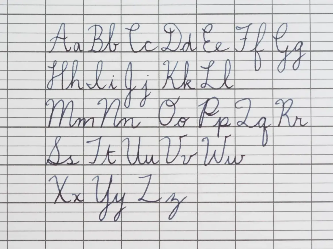 The alphabet in cursive, from A to Z, is written in neat blue ink on lined paper. The handwriting is perfect in cursive, showing each letter's formation.