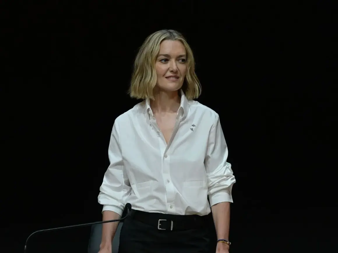 Marta Ortega Pérez, con una camisa blanca y un micrófono, sonríe ante la cámara.