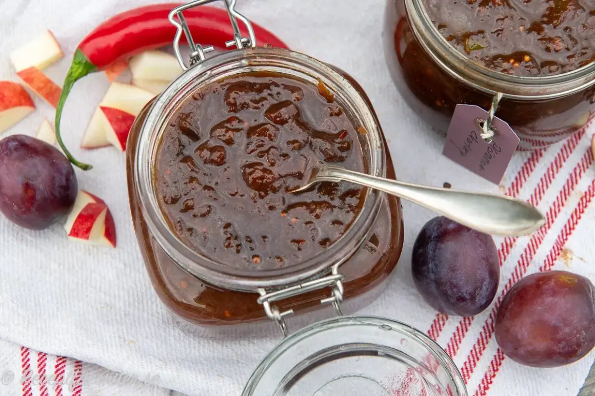 En burk med plommonchutney, perfekt för ett plommon recept. Äpplen, plommon och chili ligger bredvid.