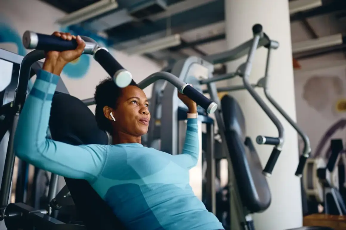Frau trainiert richtig im Fitnessstudio an einer Brustpresse. Sie konzentriert sich auf die Bewegung und hört Musik über ihre Kopfhörer.