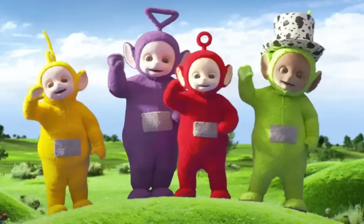 Tinky Winky, Dipsy, Laa-Laa i Po – teletubisie imiona znane dzieciom. Wesołe postacie machają do widzów na zielonej łące.