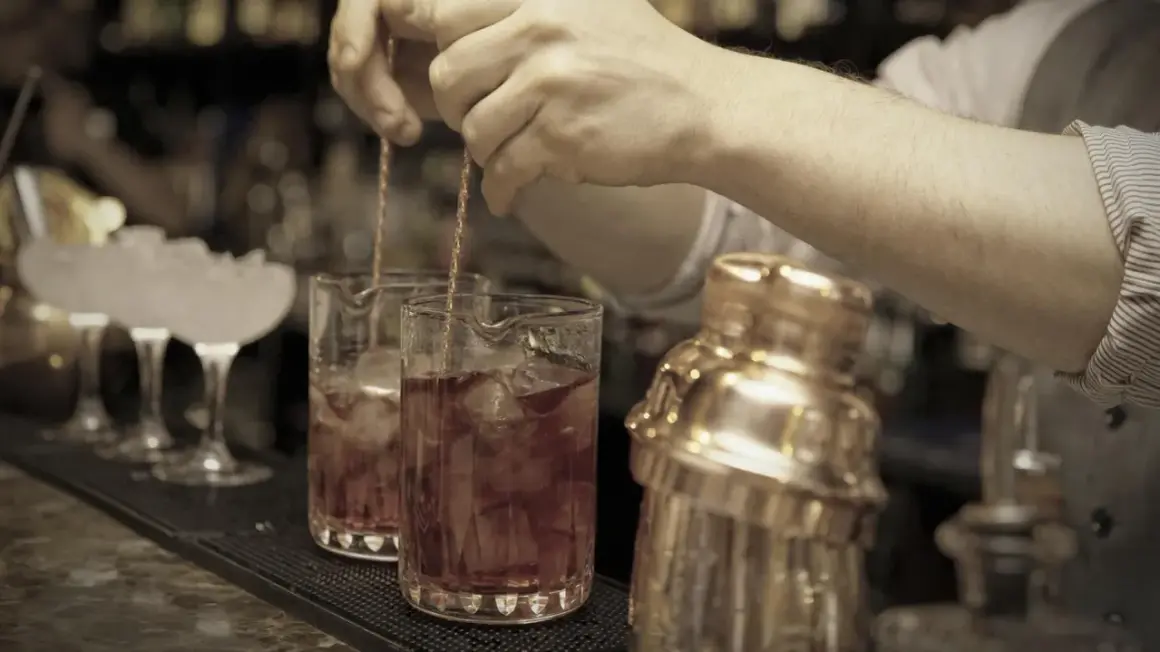 Barkeeper mixt einen roten Bier Cocktail mit Eis in einem Glas. Daneben steht ein goldener Shaker.