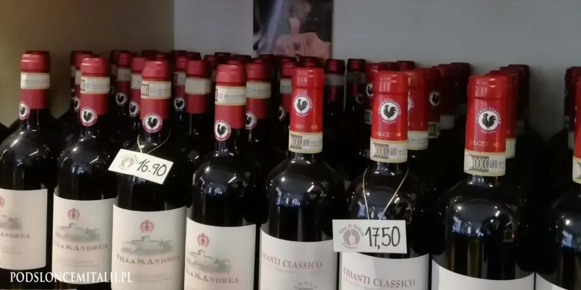 Rzędy butelek wina z kogutem na etykiecie. Na niektórych widnieją ceny: 16,90 i 17,50.