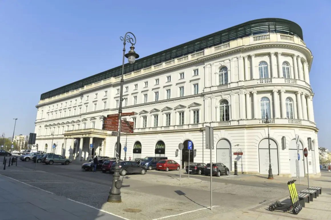 Elegancki, biały budynek hotelowy z kolumnami i łukowymi oknami, przed którym zaparkowane są samochody.