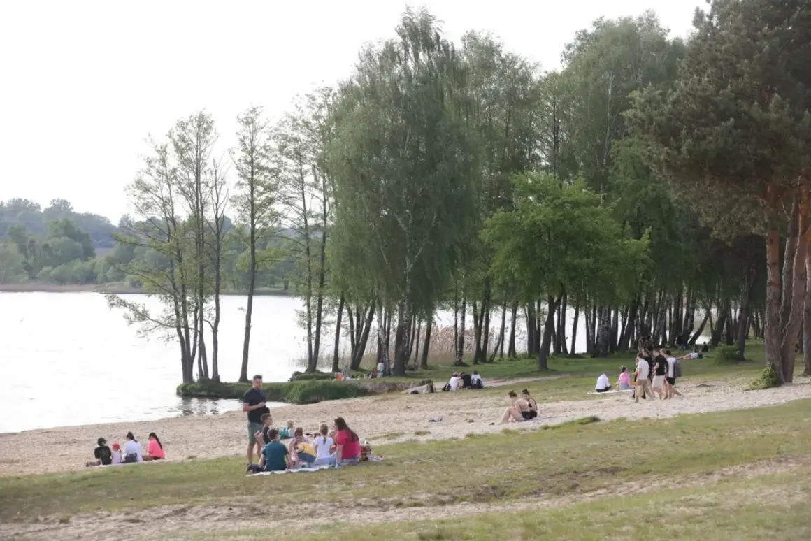 Ludzie odpoczywają na piaszczystej plaży nad jeziorem Pławniowice, ciesząc się wiosennym dniem wśród drzew.