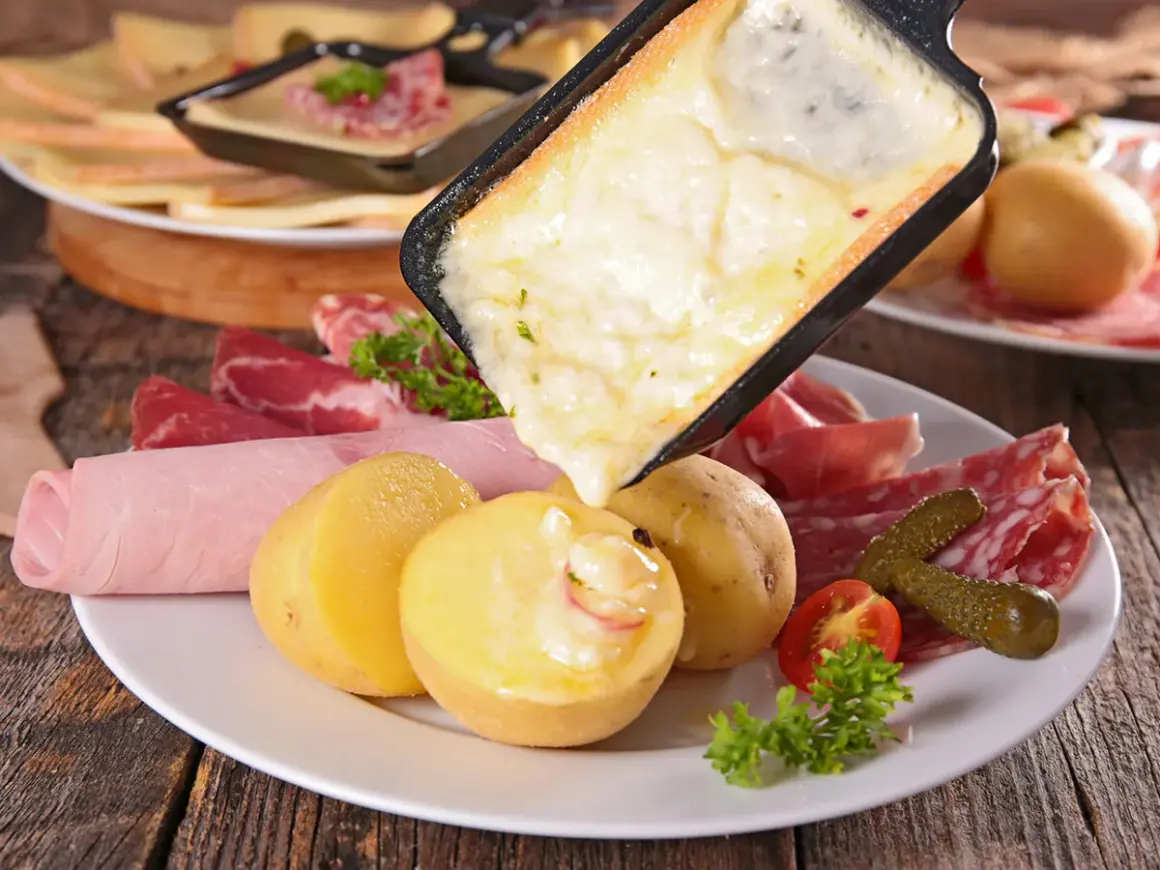 Raclette queso fundido cayendo sobre patatas, embutidos y pepinillos. ¡Una delicia para compartir!