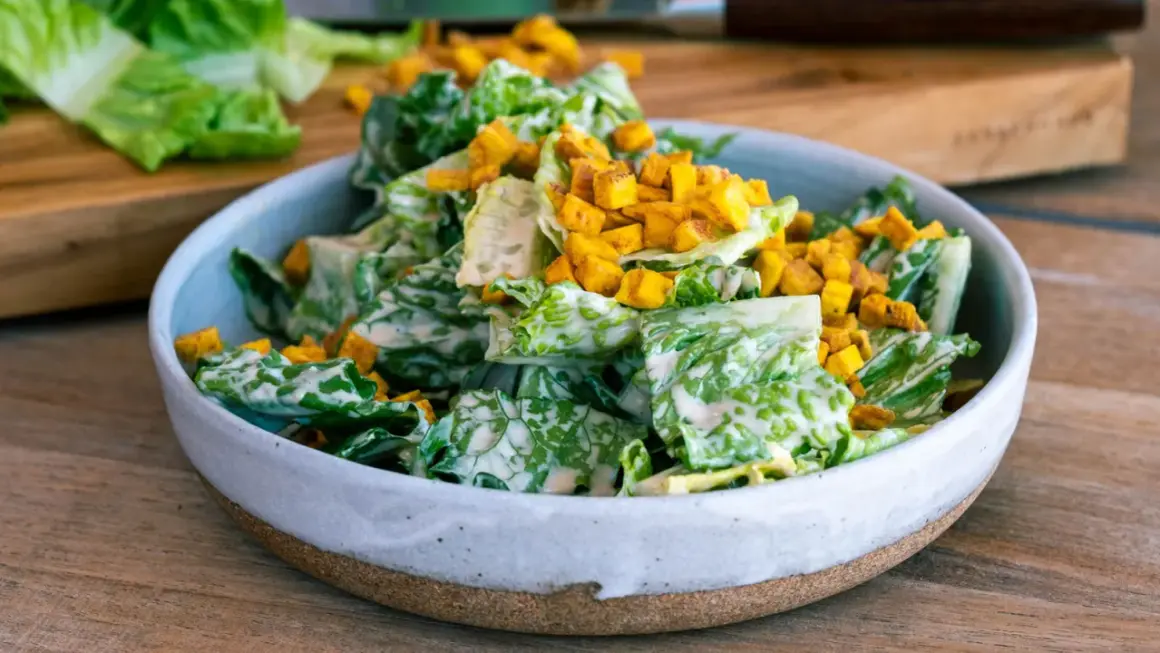 En skål med krispig romansallad, rikligt täckt med krämig caesarsallad dressing och toppad med gyllene krutonger.