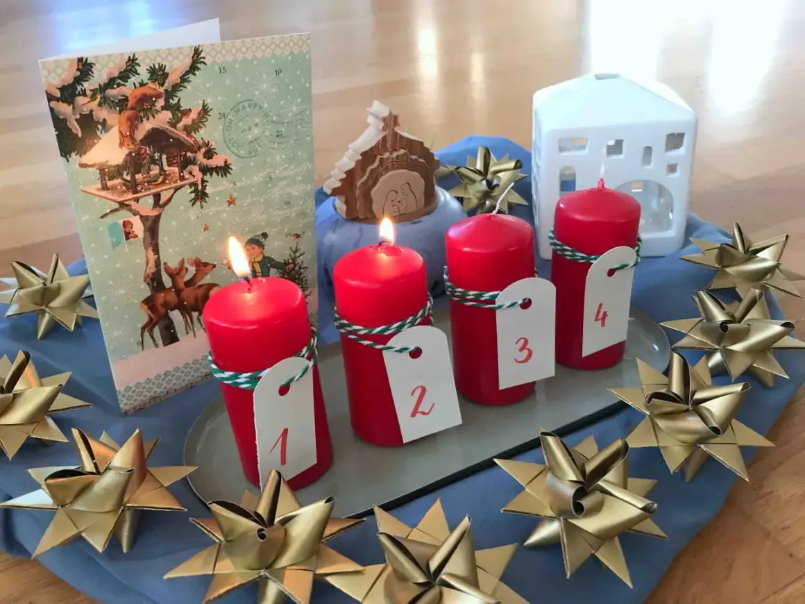 Vier rote Kerzen mit Zahlen 1-4, ein Adventskalender, ein Krippenspiel und goldene Sterne schmücken den Tisch. Perfekt für die Vorfreude auf Weihnachten in der **Advent Grundschule**.