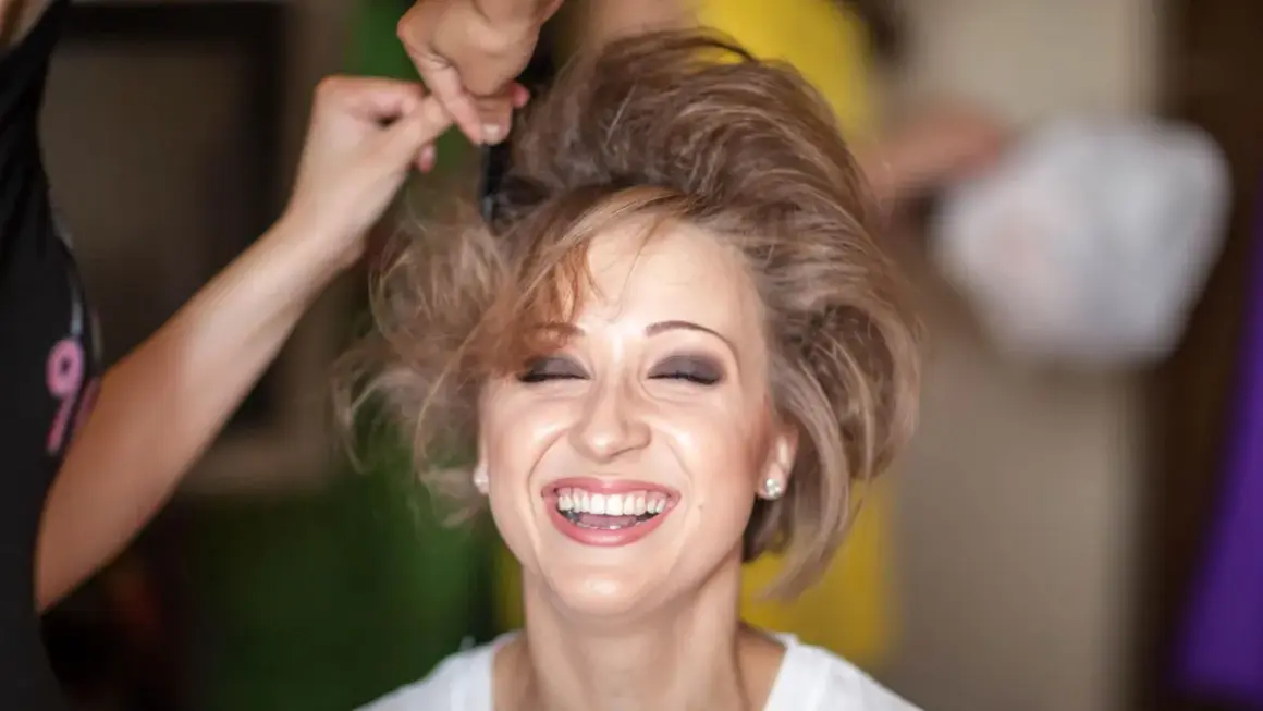 Lachende Frau, der die Haare toupiert werden für einen voluminösen Look.
