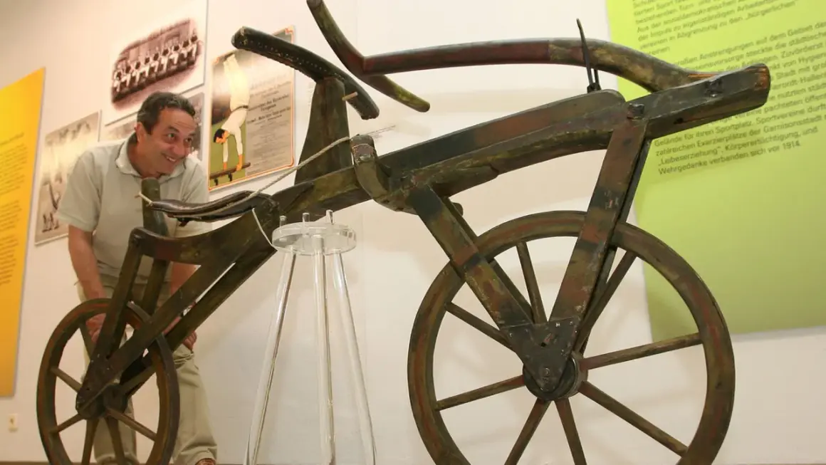 Ein Mann betrachtet das erste Fahrrad der Welt, ein hölzernes Gefährt ohne Pedale, das an ein Laufrad erinnert.