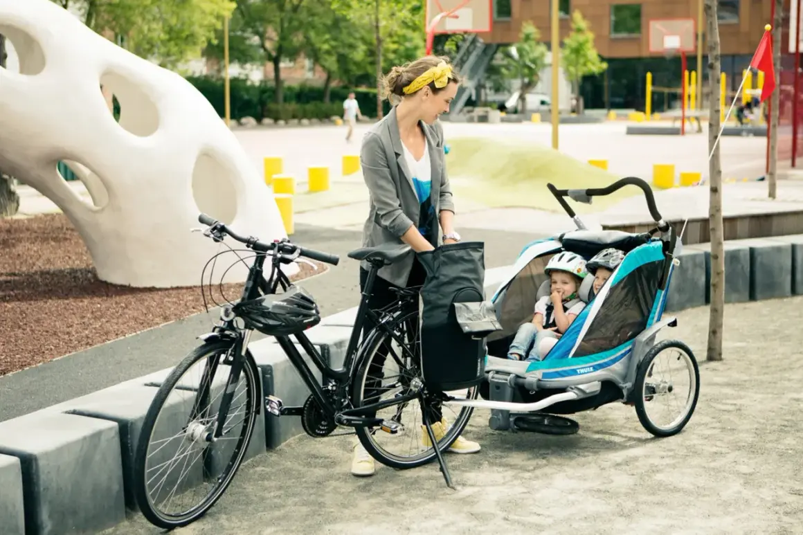 Frau mit Fahrrad und Kinderanhänger, bereit für eine Ausfahrt. Sie genießt das Fahrrad fahren, auch in der Schwangerschaft.